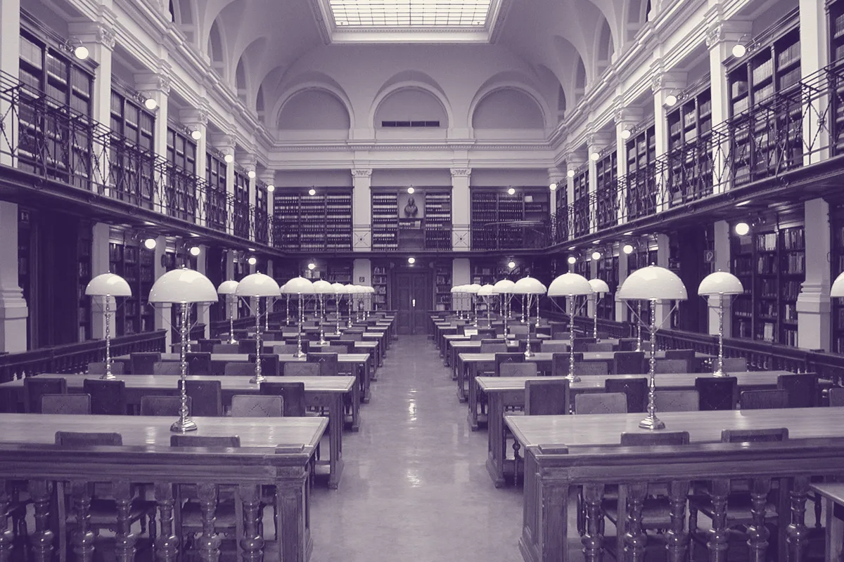 Une salle de lecture symétrique, alignement de lampes sur les tables de travail.